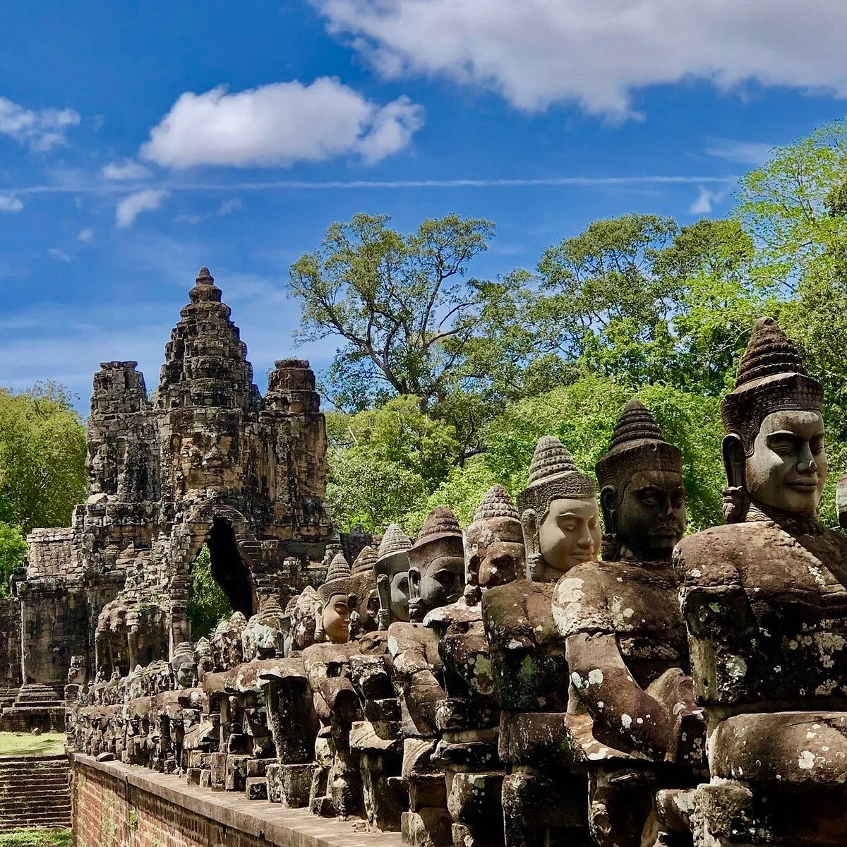 Porte d'Angkor Thom surmontée de visages de pierre, et chaussée bordée de statues de divinités